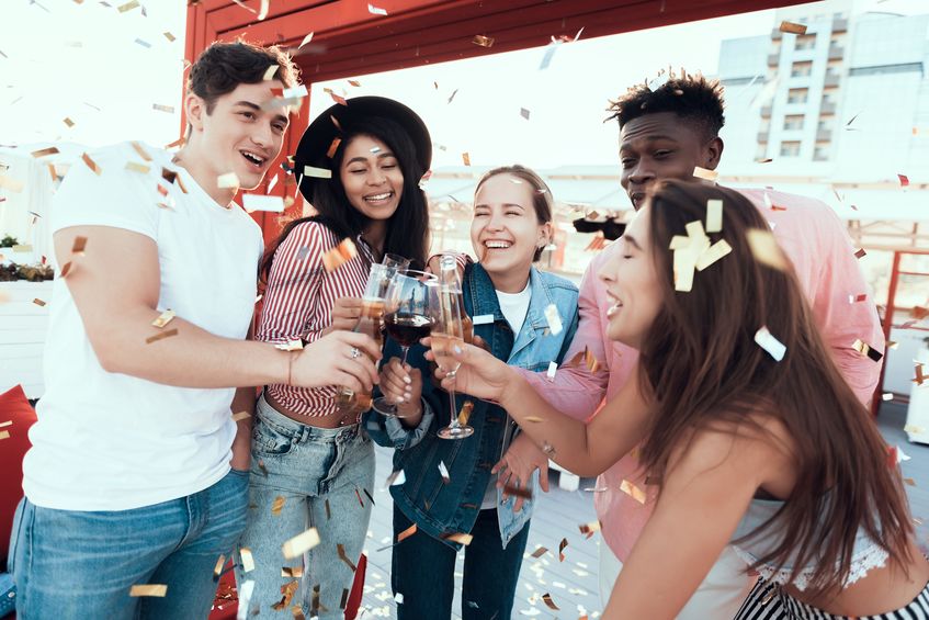 group of friends drinking Champaign and laughing together on boat with confetti